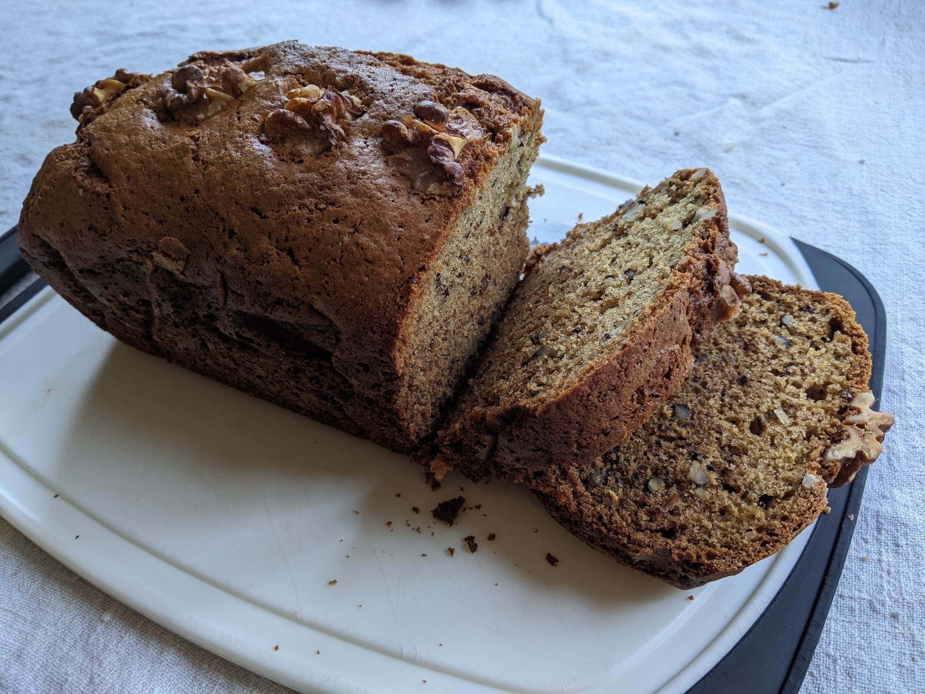 loaf of banana bread with two slices cut on a white cutting board 
